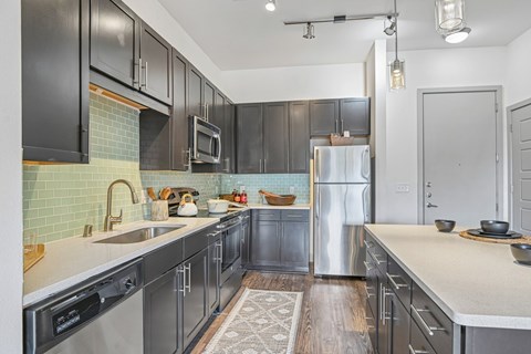 A kitchen with black cabinets and a stainless steel refrigerator.
