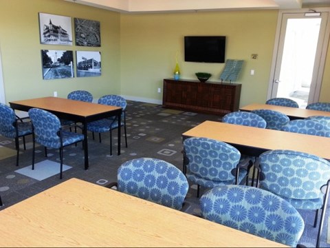 A room with tables and chairs and a television on the wall.
