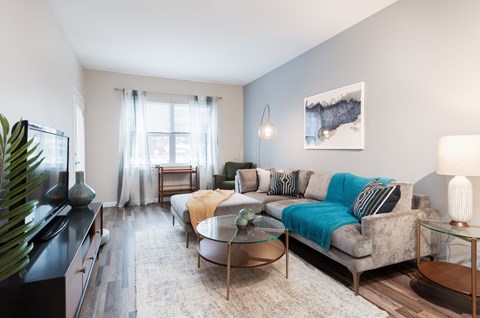 A living room with a grey couch, a glass table, and a painting on the wall.