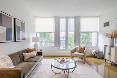 A living room with a grey couch, a glass table, and a painting on the wall.