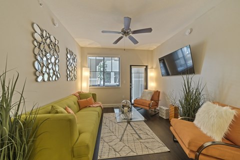 A living room with a yellow couch, a coffee table, and a flat screen TV mounted on the wall.