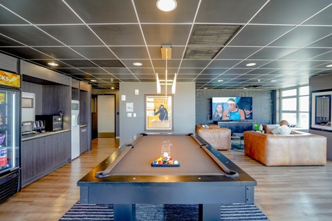 A pool table is in the middle of a room with a bar and a couch.