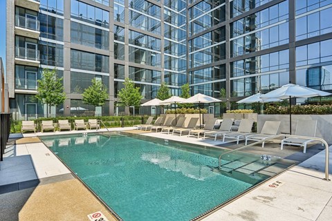 an outdoor pool with lounge chairs and umbrellas next to a tall building
