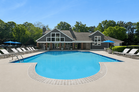 A large swimming pool in front of a house with a blue sky in the background.