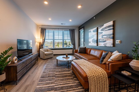A living room with a brown leather couch and a coffee table in front of a large window.