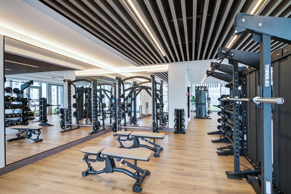 Fitness center with strength training equipment, free weighs and benches in front of wall-to-wall mirrors
