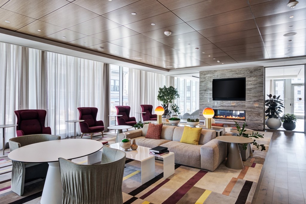 Resident lounge with multiple soft seating areas, tables and chairs and fireplace with mounted TV above surrounded by floor-to-ceiling windows