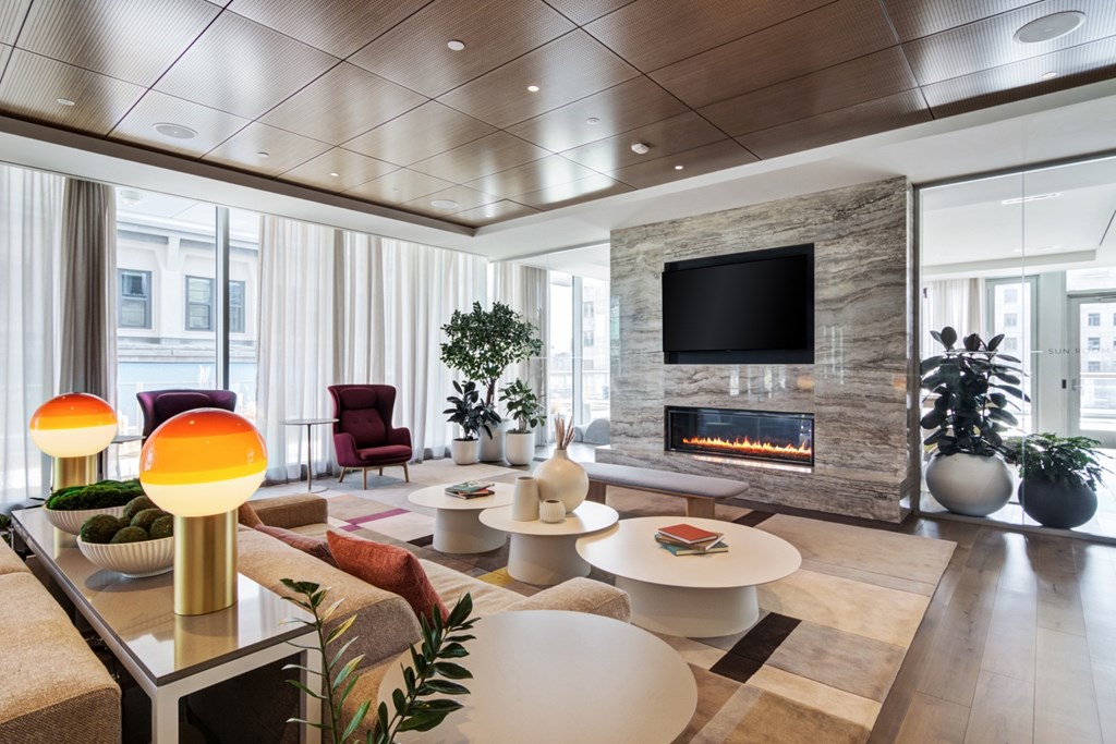 Resident lounge with multiple soft seating areas, tables and chairs and fireplace with mounted TV above surrounded by floor-to-ceiling windows