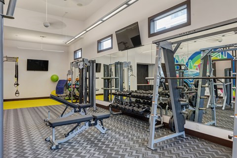 A gym with a variety of equipment including a weight bench, a cable machine, and a squat rack.