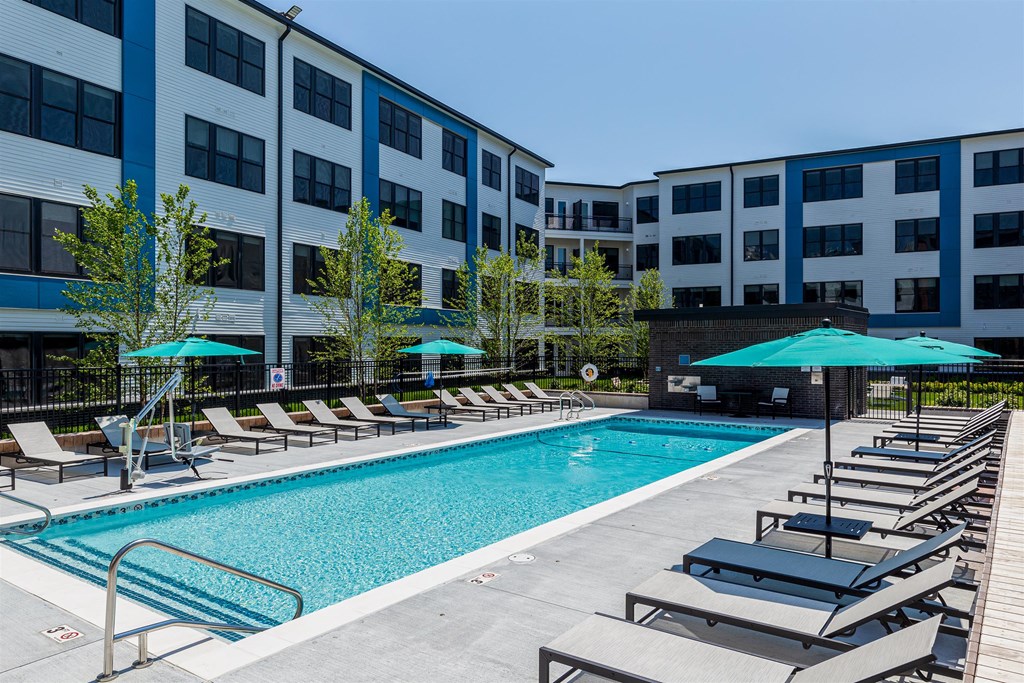 a pool with lounge chairs and umbrellas in front of an apartment building