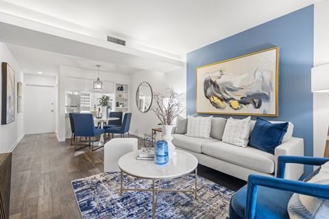 A living room with a white couch, blue chairs, and a painting on the wall.