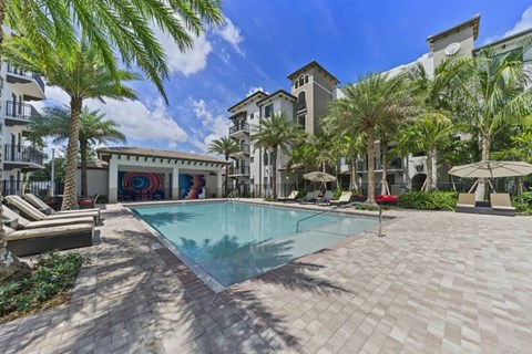 A pool surrounded by palm trees and lounge chairs.