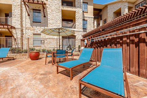 A patio with blue chairs and a table with a red pot.
