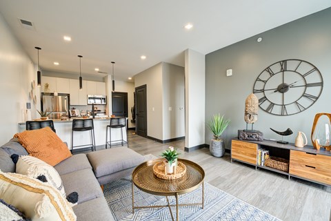 A living room with a grey couch and a large clock on the wall.