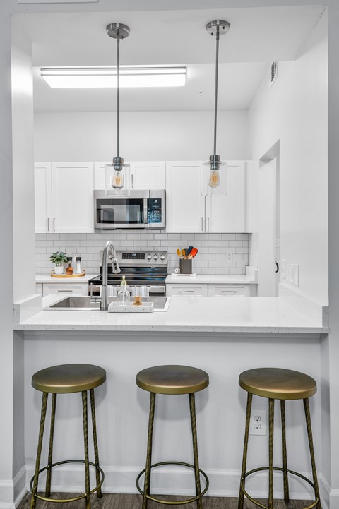 A kitchen with white cabinets and a white countertop with a microwave and a sink.