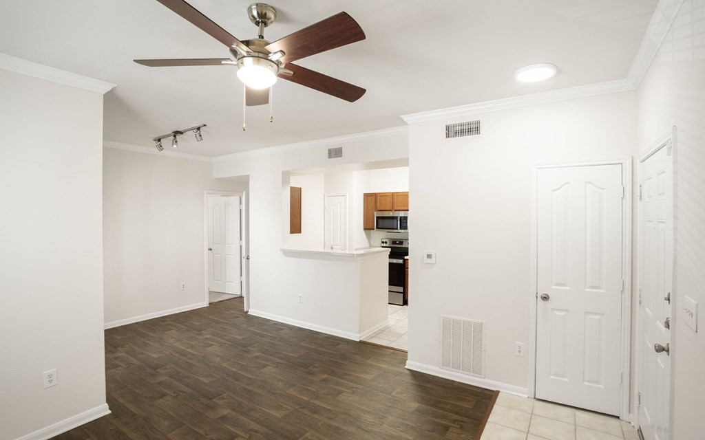 a living room with a ceiling fan and a kitchen in the background
