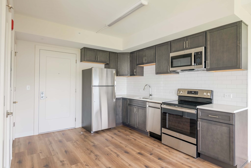 an empty kitchen with stainless steel appliances and wooden floors