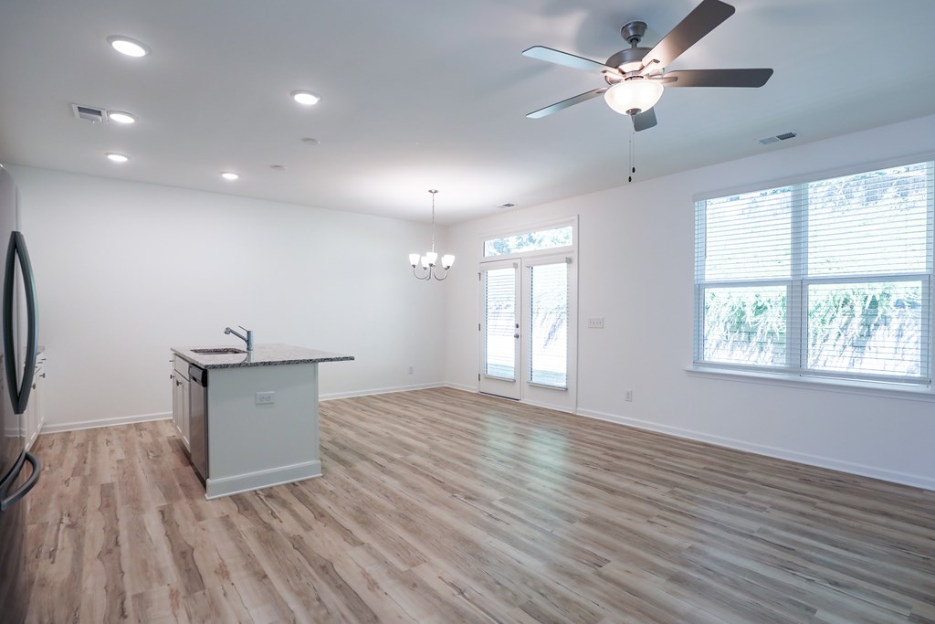 an empty living room with a ceiling fan and a kitchen