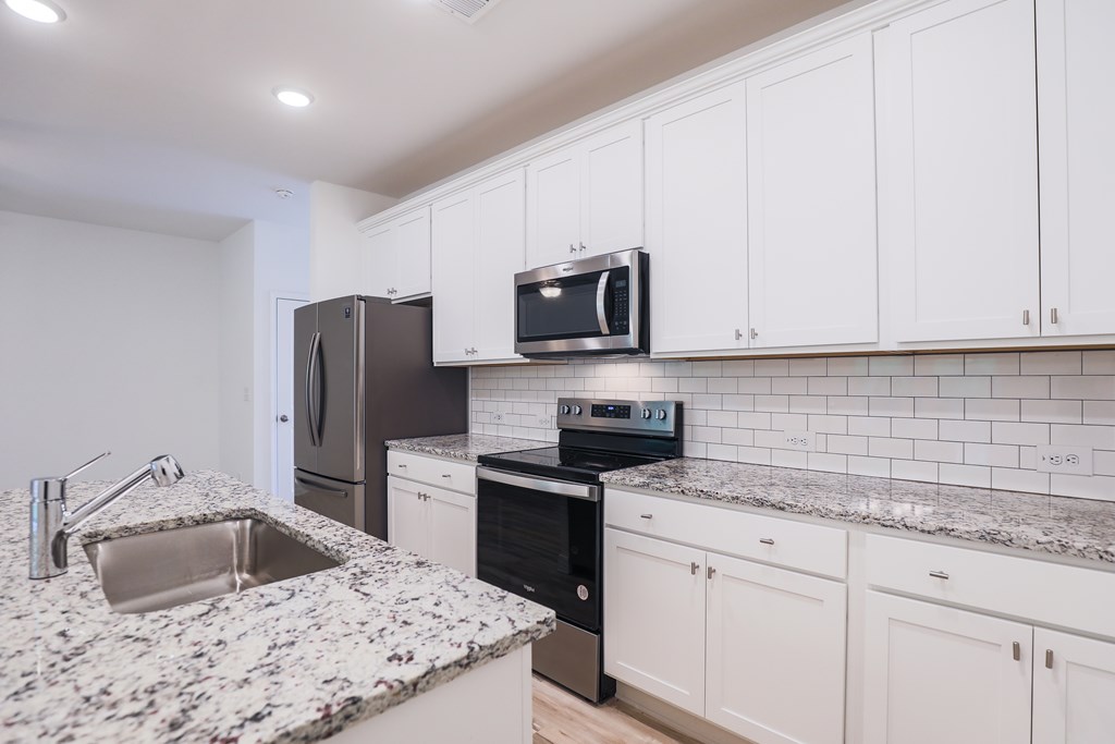 a kitchen with white cabinets and granite counter tops and black appliances