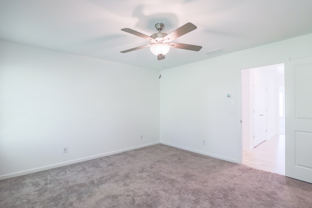 an empty room with a ceiling fan and a carpet