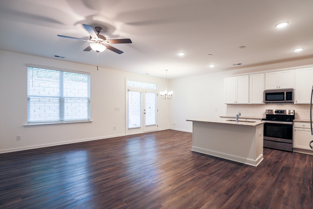 an empty living room with a kitchen and a ceiling fan