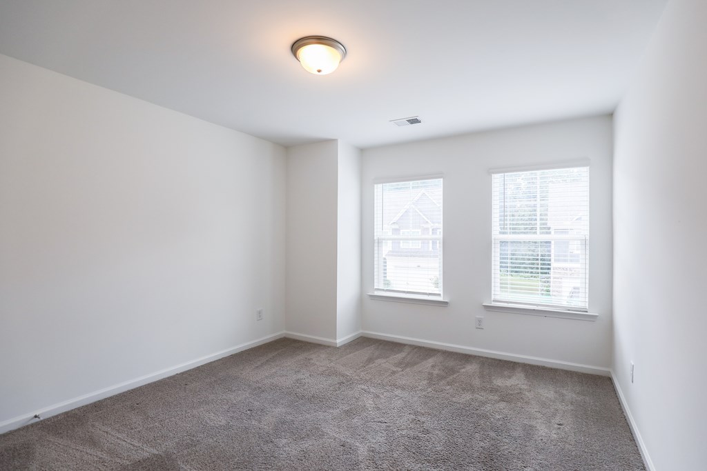 an empty living room with carpet and two windows