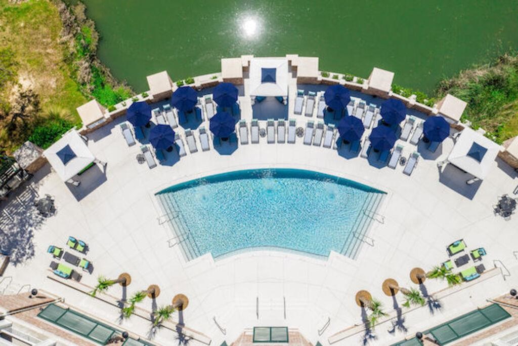 an aerial view of a swimming pool with blue umbrellas and chairs around it