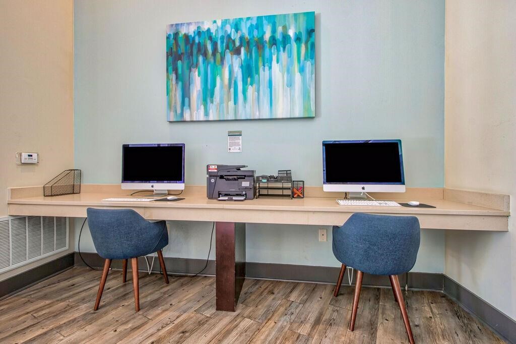 a desk with two computers and a painting on the wall