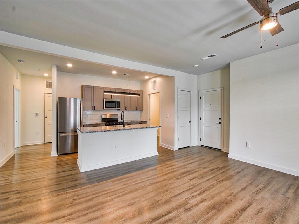 an empty living room with a kitchen with stainless steel appliances