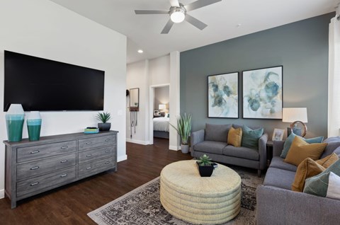 A living room with a grey couch, a round ottoman, and a flat screen TV mounted on the wall.