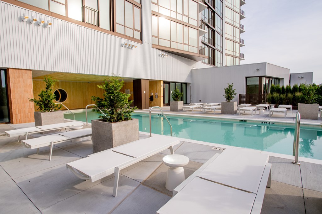 a pool with white lounge chairs and tables in front of a building