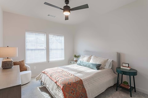A bedroom with a bed, a ceiling fan, and a small table with a plant on it.