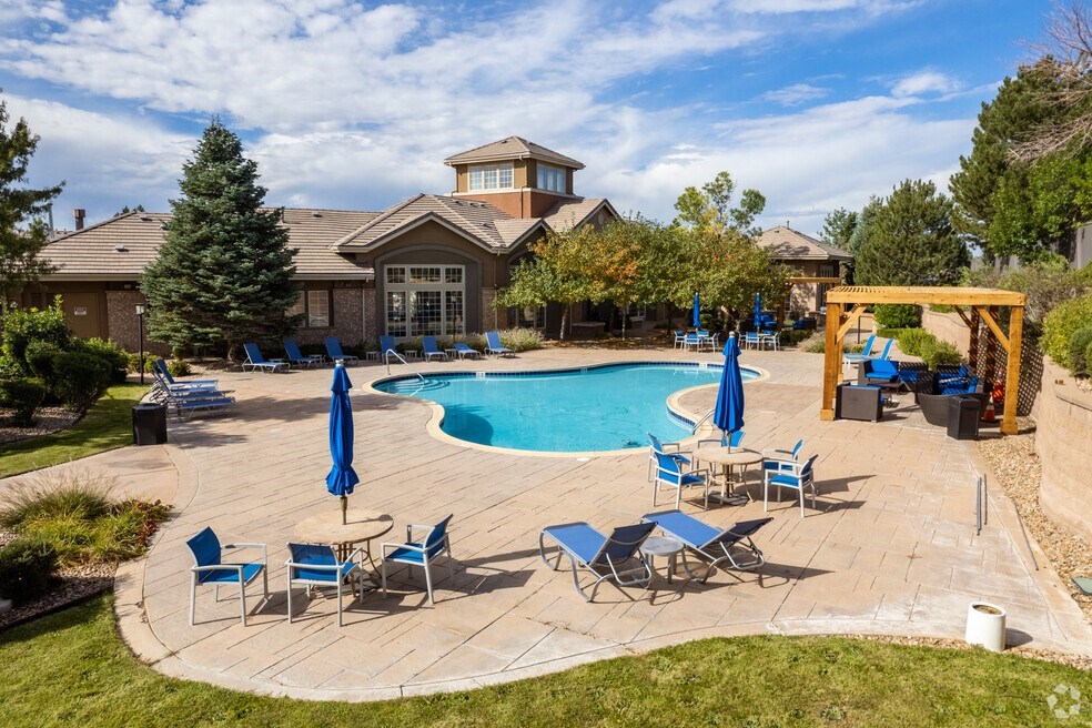 South Aurora, CO, Apartments for Rent - Sonoma Resort at Saddle Rock - Pool with Lounge Seats, Umbrellas, Tables, Chairs, Pergola, and Surrounding Trees.