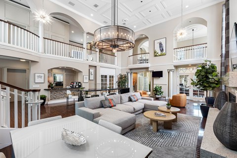 A spacious living room with a white sofa set and a chandelier hanging from the ceiling.
