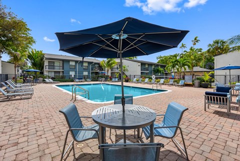 A patio with a table, chairs and an umbrella overlooking a pool.