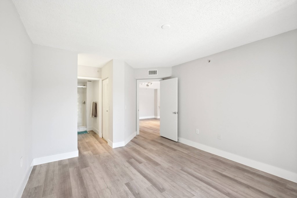A room with white walls and wooden flooring with a door on the right.