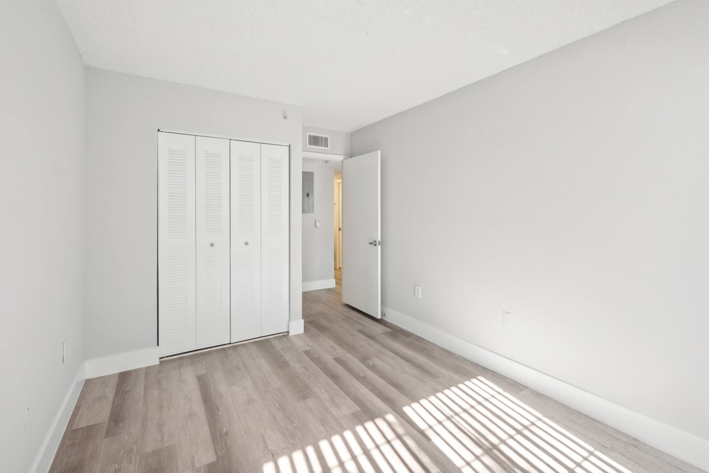 A room with white walls and a wooden floor with sunlight coming through the window.