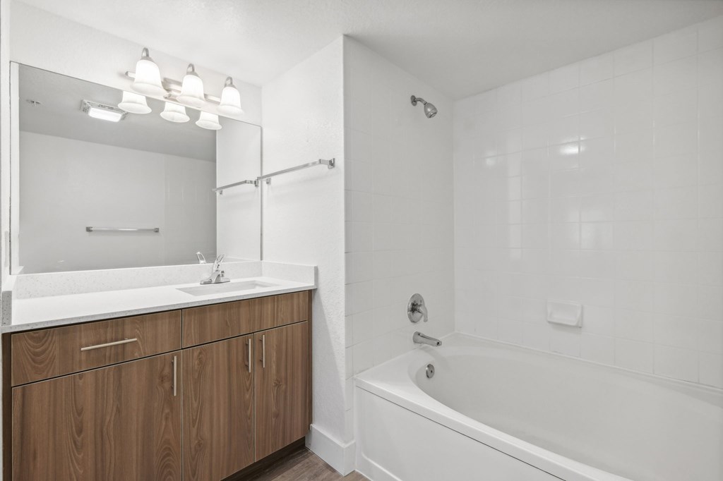 A white bathroom with a wooden vanity and a white bathtub.