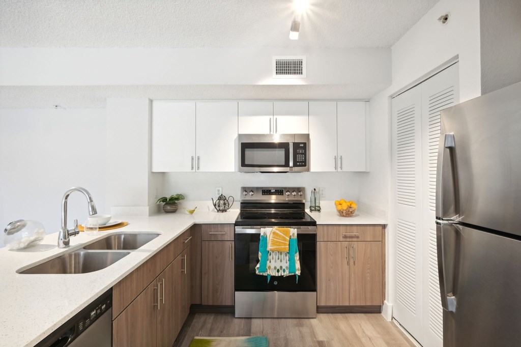 A modern kitchen with a stainless steel refrigerator, a stove with a towel on it, and a sink with a bowl on it.