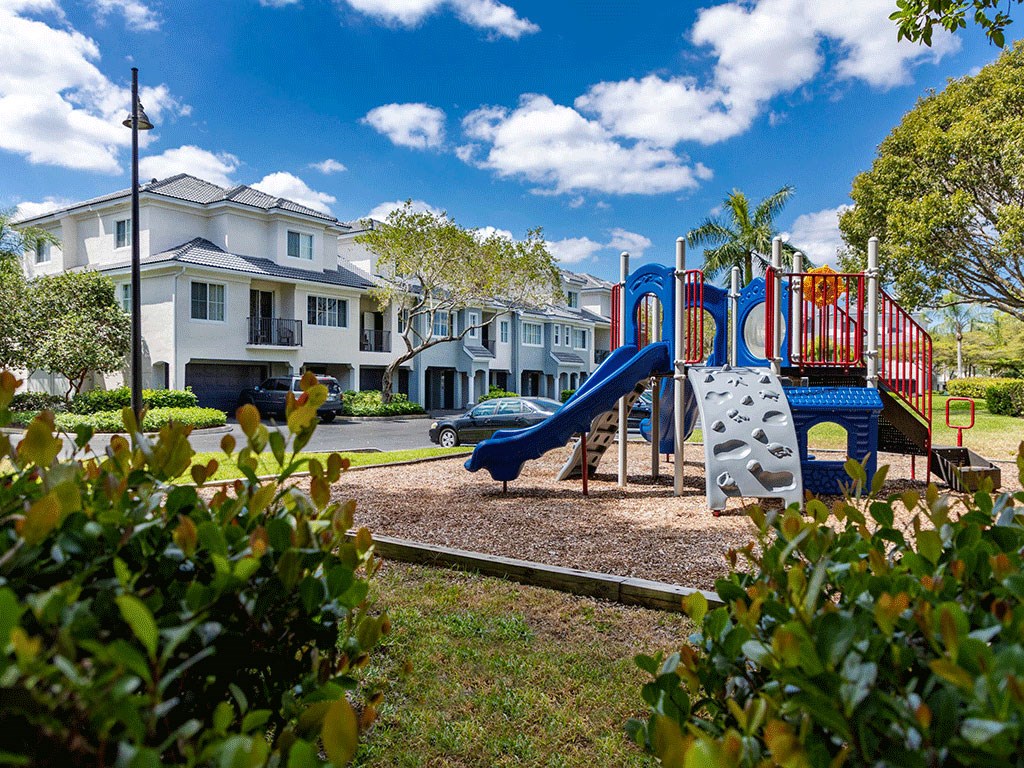 a playground with a blue slide in a park in front of houses