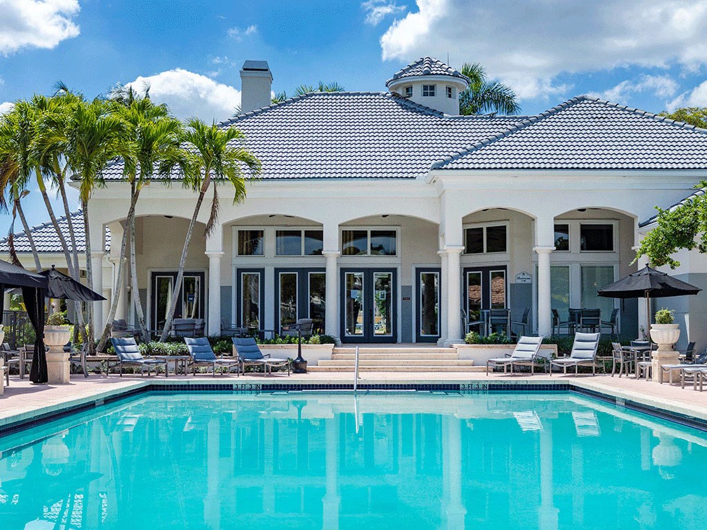 a large swimming pool in front of a white house with palm trees