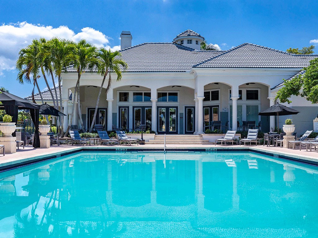 a large swimming pool in front of a white house with palm trees