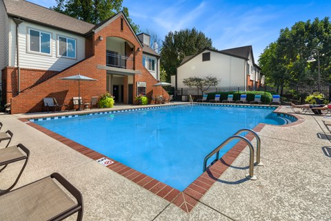 A swimming pool surrounded by a brick border and lounge chairs.