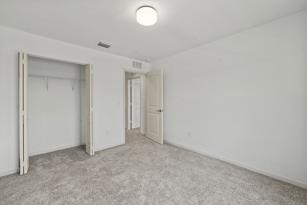 a bedroom with white walls and carpet and a door to a closet