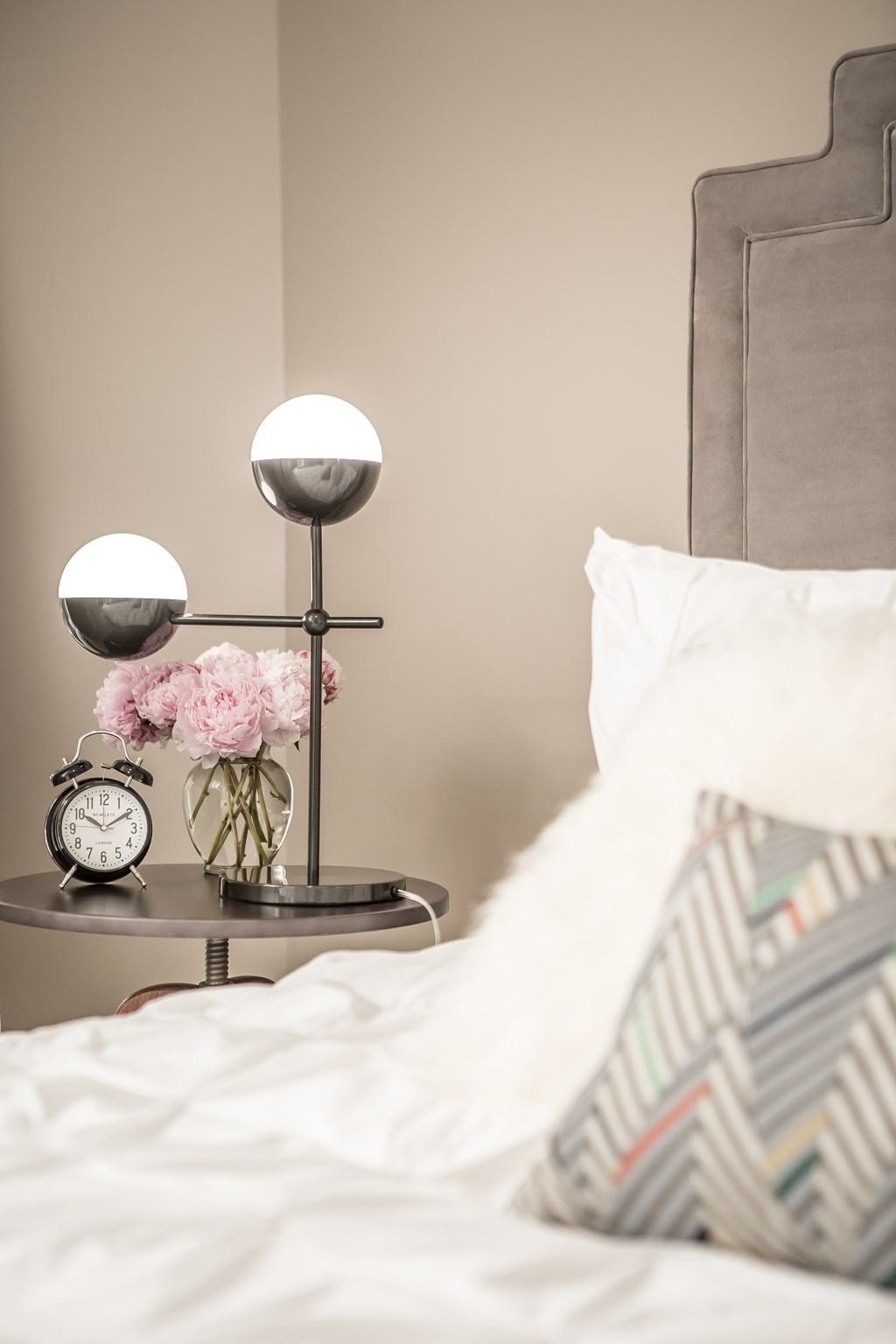 a bed with white sheets and a nightstand with a clock and a vase
