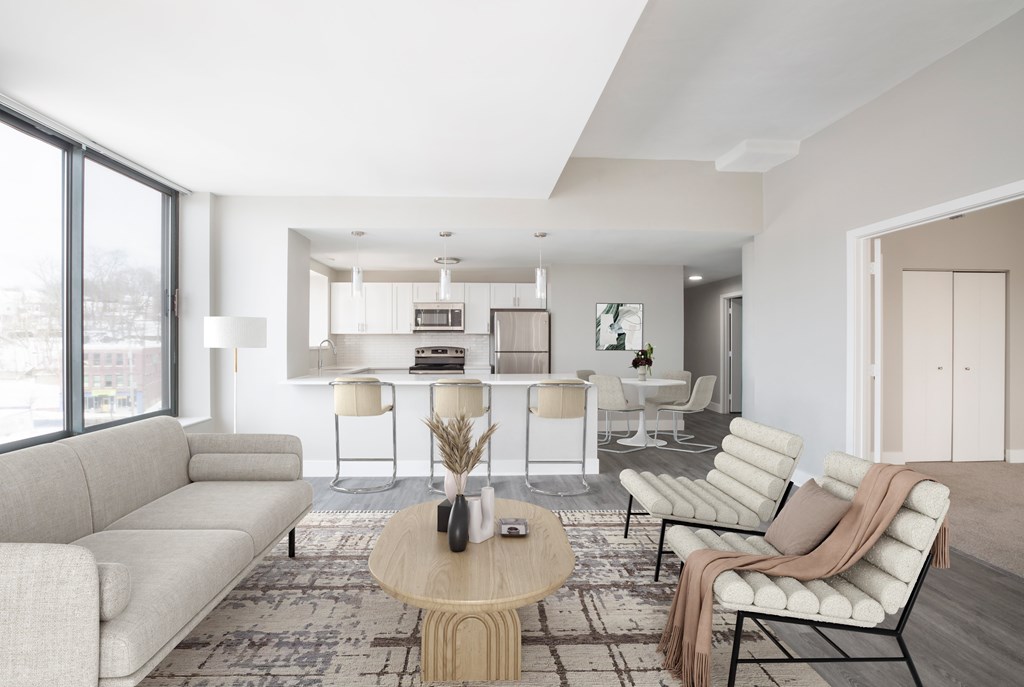 A modern living room with a large window and a dining area in the background.