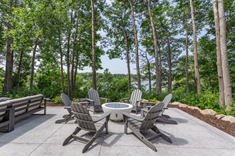 a patio with a firepit and chairs with a view of the water - Photo Gallery
