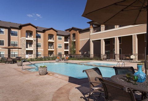 A pool area with chairs and umbrellas in front of apartment buildings.