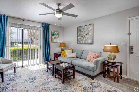 A living room with a grey couch, a rug, a table with a lamp and a painting on the wall.