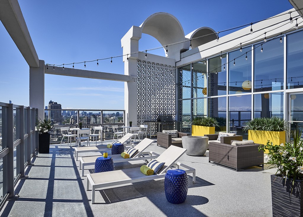 One Bedroom Apartments in Chicago Lakeview, IL - 30th Floor Rooftop Sun Deck, Lound Seating, Pillows, Modern Decor, Potted Plants, BBQ Grill, And City Views.